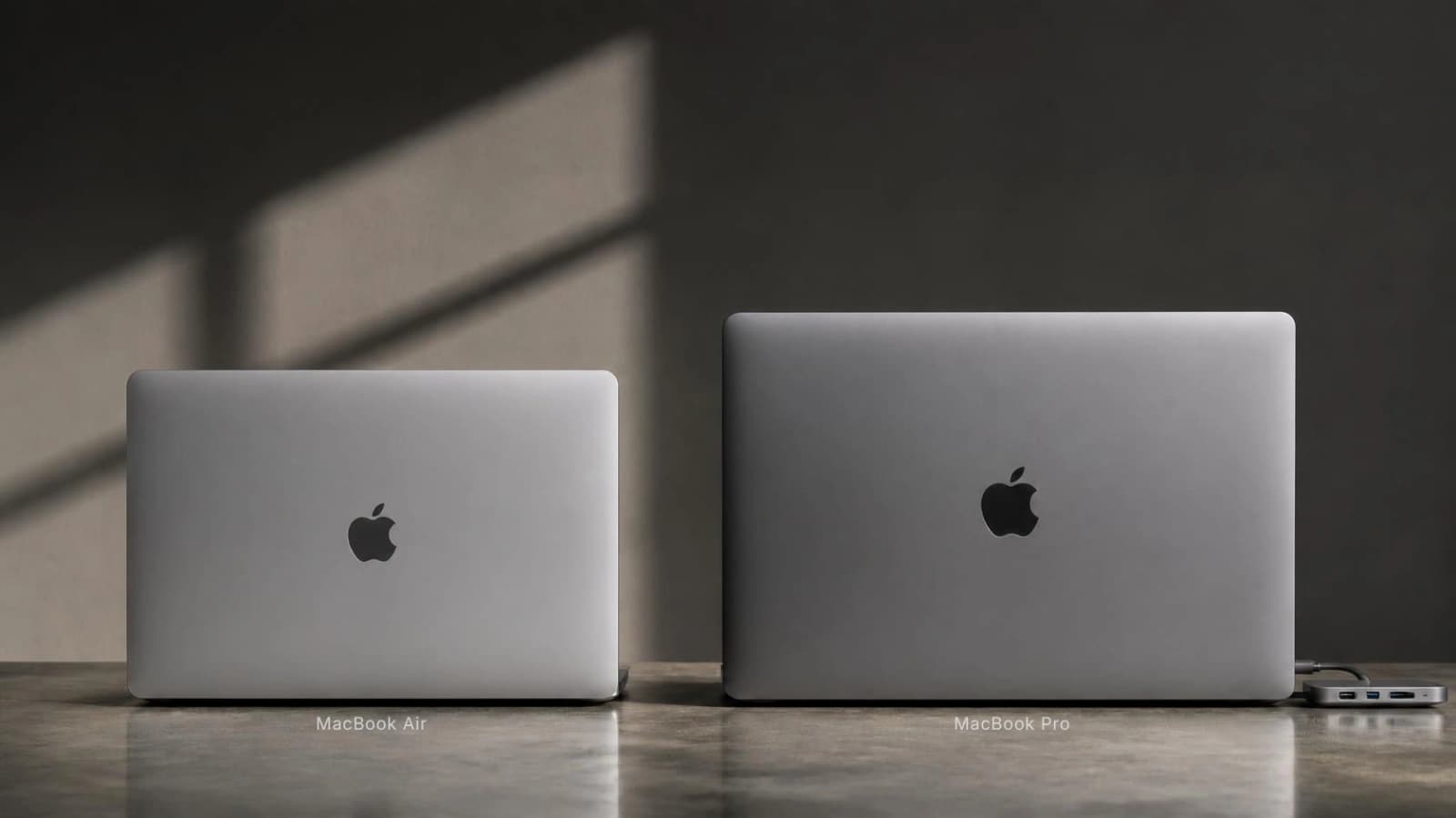 MacBook Air and larger MacBook Pro side by side on a desk, seen from the back to compare their size